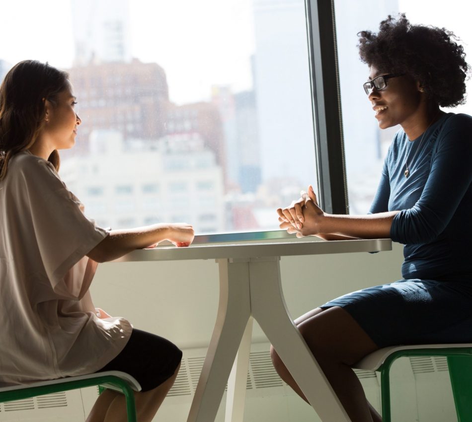 Two Women Sitting In Front Of A Window Talking